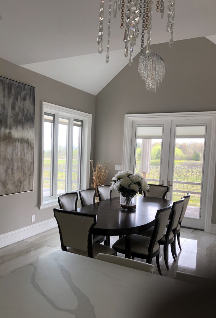 A living room with two windows and a dining table with 8 chairs and flower bouquet.