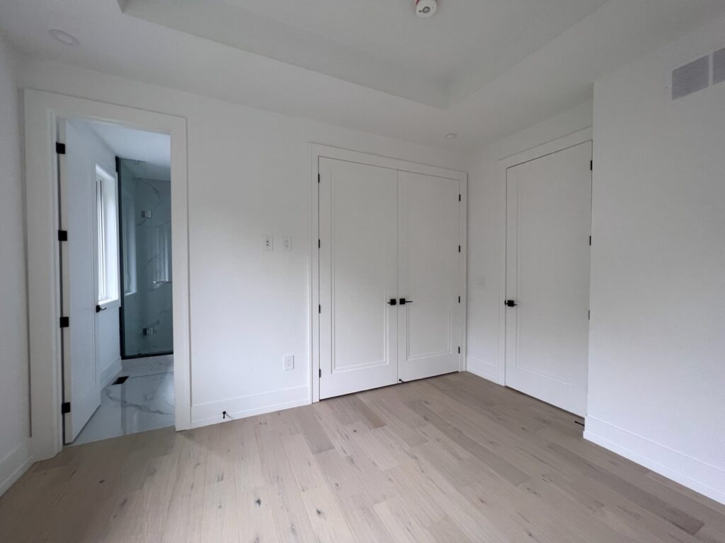 A bedroom in a custom house with a bathroom and a modern build-in closet.