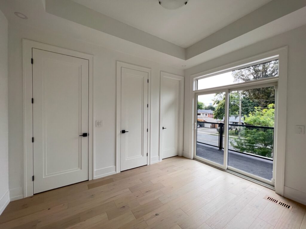 Minimalistic bedroom with a large window and two closet doors painted white.
